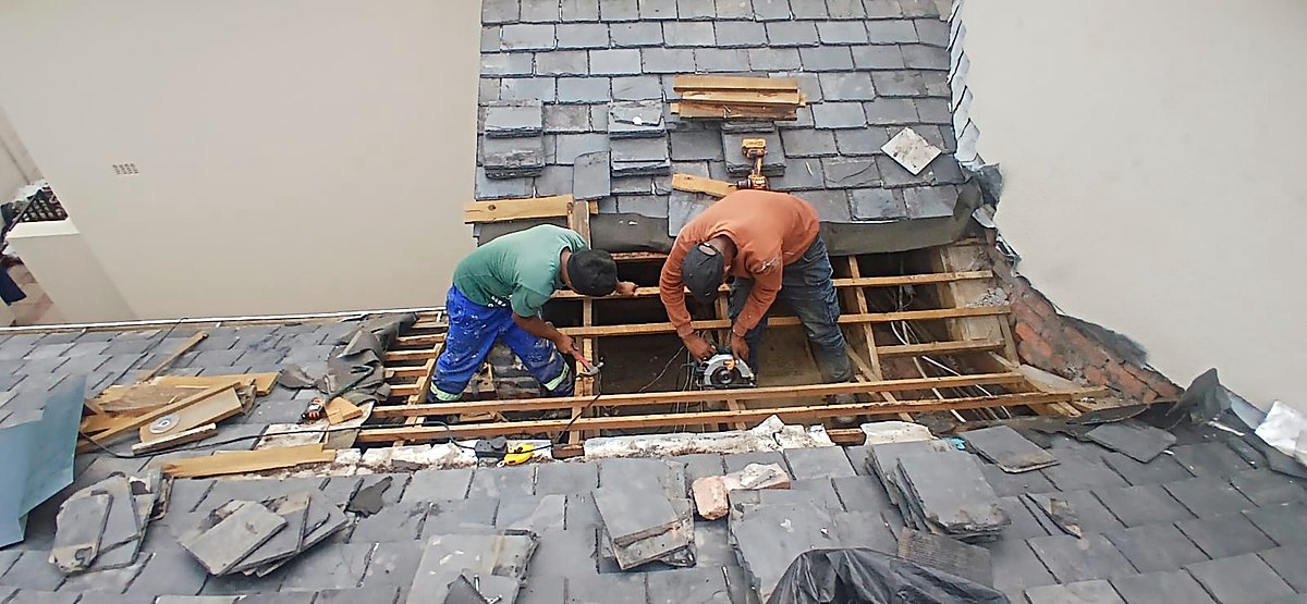 Two roofers repairing a slate roof valley against a plastered wall
