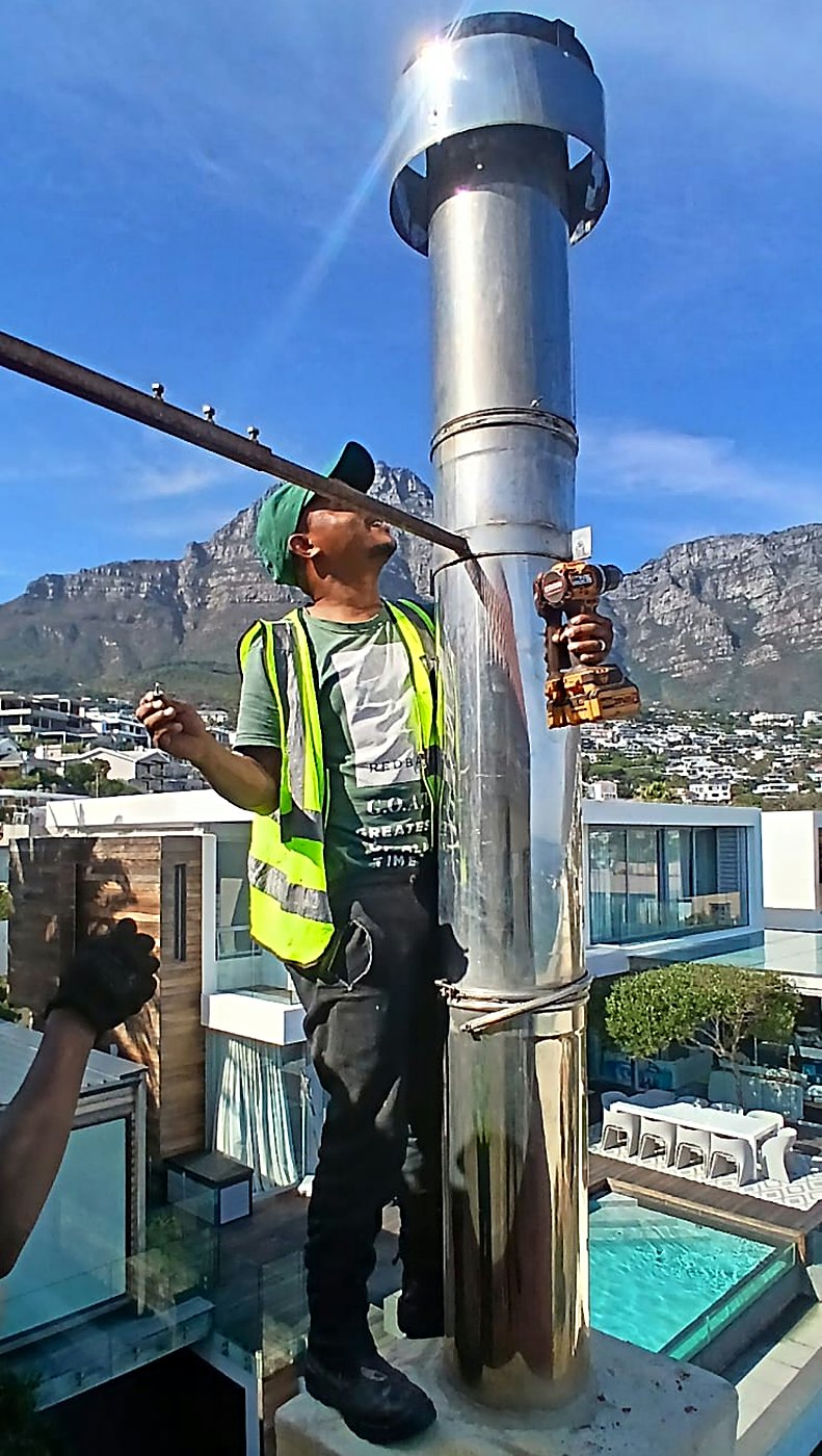 Team member fitting a stainless steel flue on a rooftop with Table Mountain behind