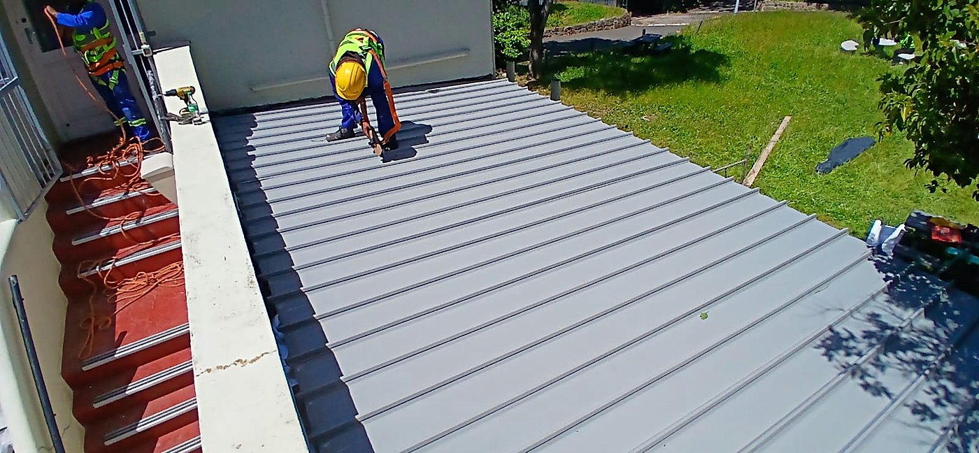 Completed grey metal sheeted roof with a roofer finishing the last fixings